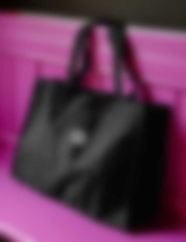 A black rectangular bag sitting on a magenta bench, with customisation option in the middle