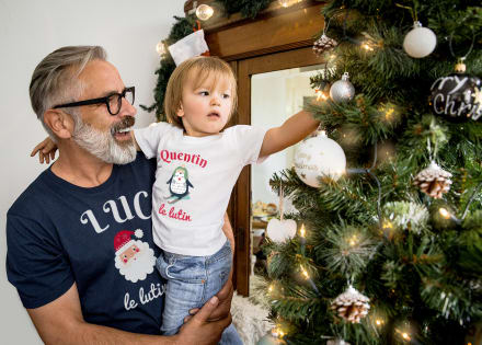 Grand-père porte son petit fils dans les bras. Ils décorent le sapin de Noël avec leur t-shirt personnalisé